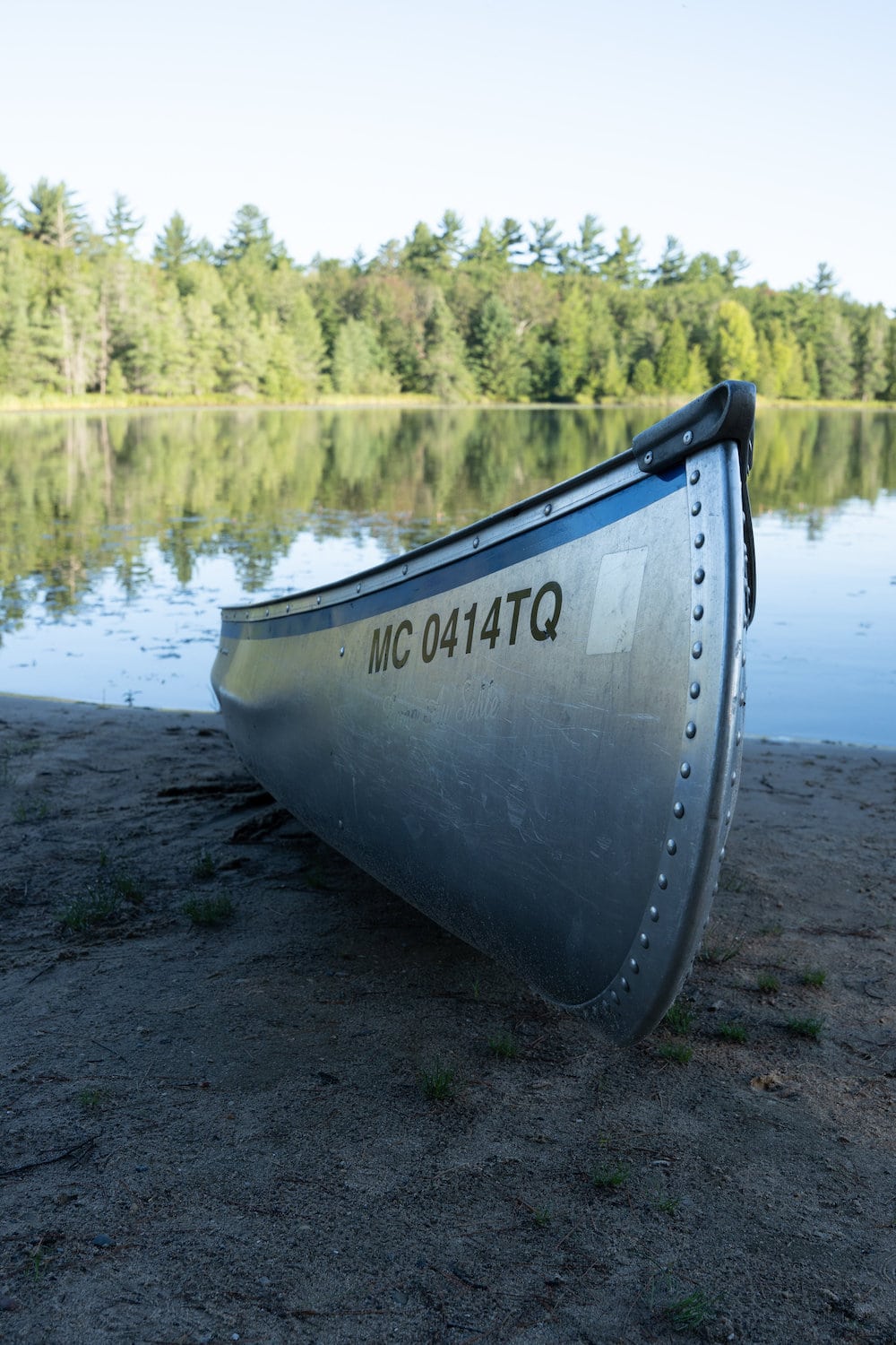 Photograph of a aluminum canoe the bank of a lake, un edited, color and contrast are flat