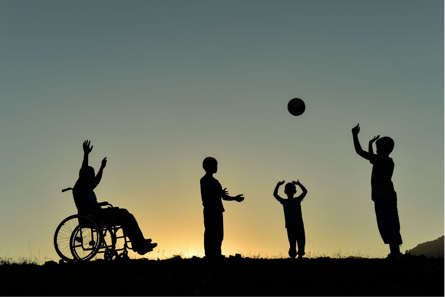 Kids silhouetted playing catch.     