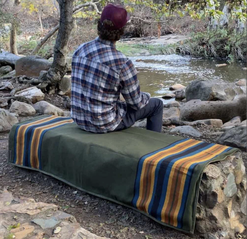 Man sitting on the Waxed Canvas Blanket blanket near a stream.